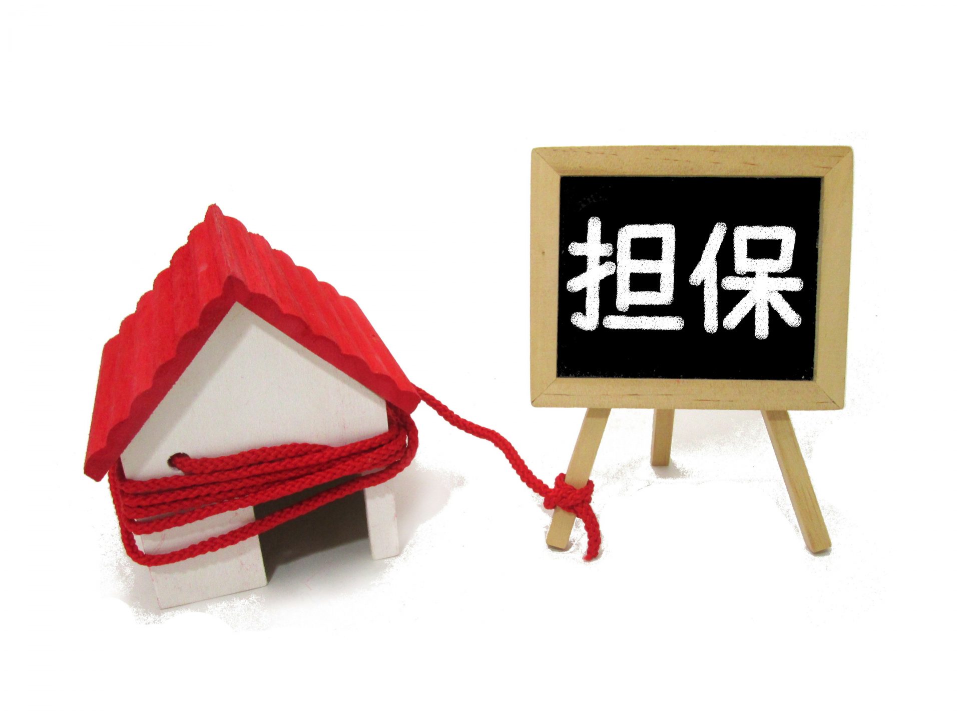 赤い屋根の家の模型に赤い縄がぐるぐる巻きにされ、その縄が「担保」と書かれた黒板のイーゼルの脚につながれている
